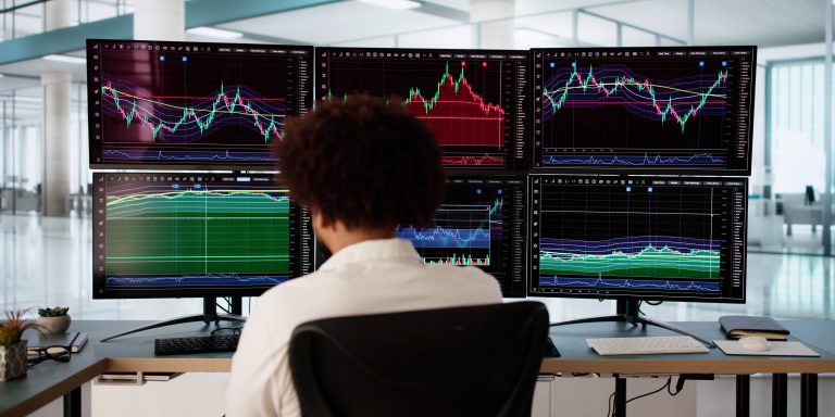 African American stock market broker analyzing graphs on multiple screens